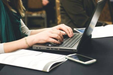 Compression des PDF sur les portables : les meilleurs outils pour les utilisateurs modernes Adult woman typing on a laptop at a desk with a smartphone and documents.