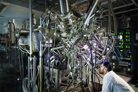 Un chercheur en matériaux de Sandia observe à travers la fenêtre d'un réacteur à épitaxie par jets moléculaires, destiné à la fabrication de plaques de refroidissement photoniques.