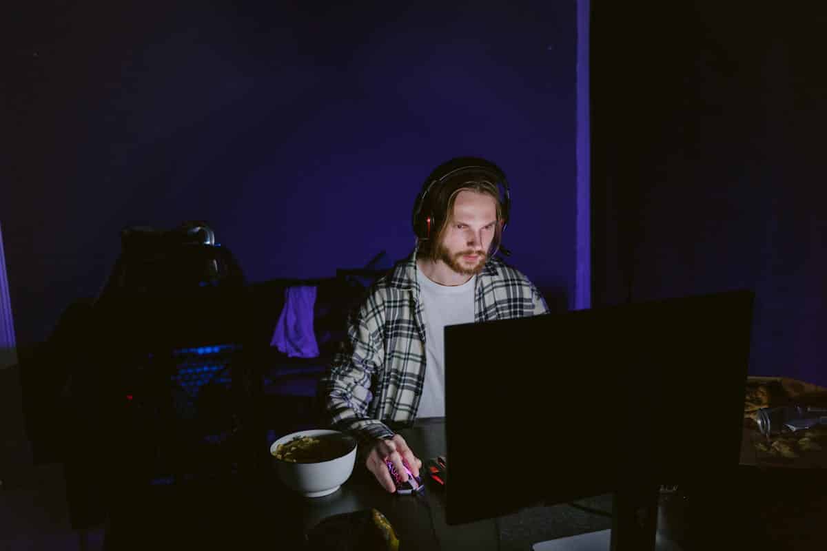 Le jeu de niveau supérieur : comment les retours des fans stimulent les plus grandes innovations du jeu vidéo A focused man playing video games on a computer at night with a headset.