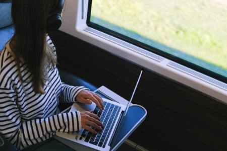 Optimisez votre expérience : guide complet du streaming musical en haute résolution Person with headphones using laptop on a train, symbolizing remote work and digital nomad lifestyle.