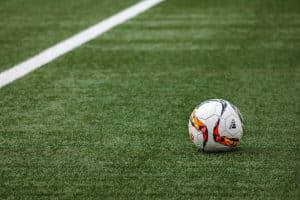 Les 5 Meilleures Applications Pour Regarder Des Matchs De Football En Direct : Guide Pratique 2025 A vibrant soccer ball resting on a pristine grass field beside a white sideline.