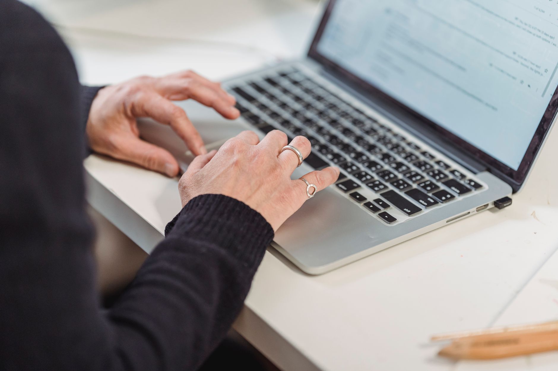 Mains d’une personne utilisant le clavier d’un ordinateur portable sur un bureau blanc.