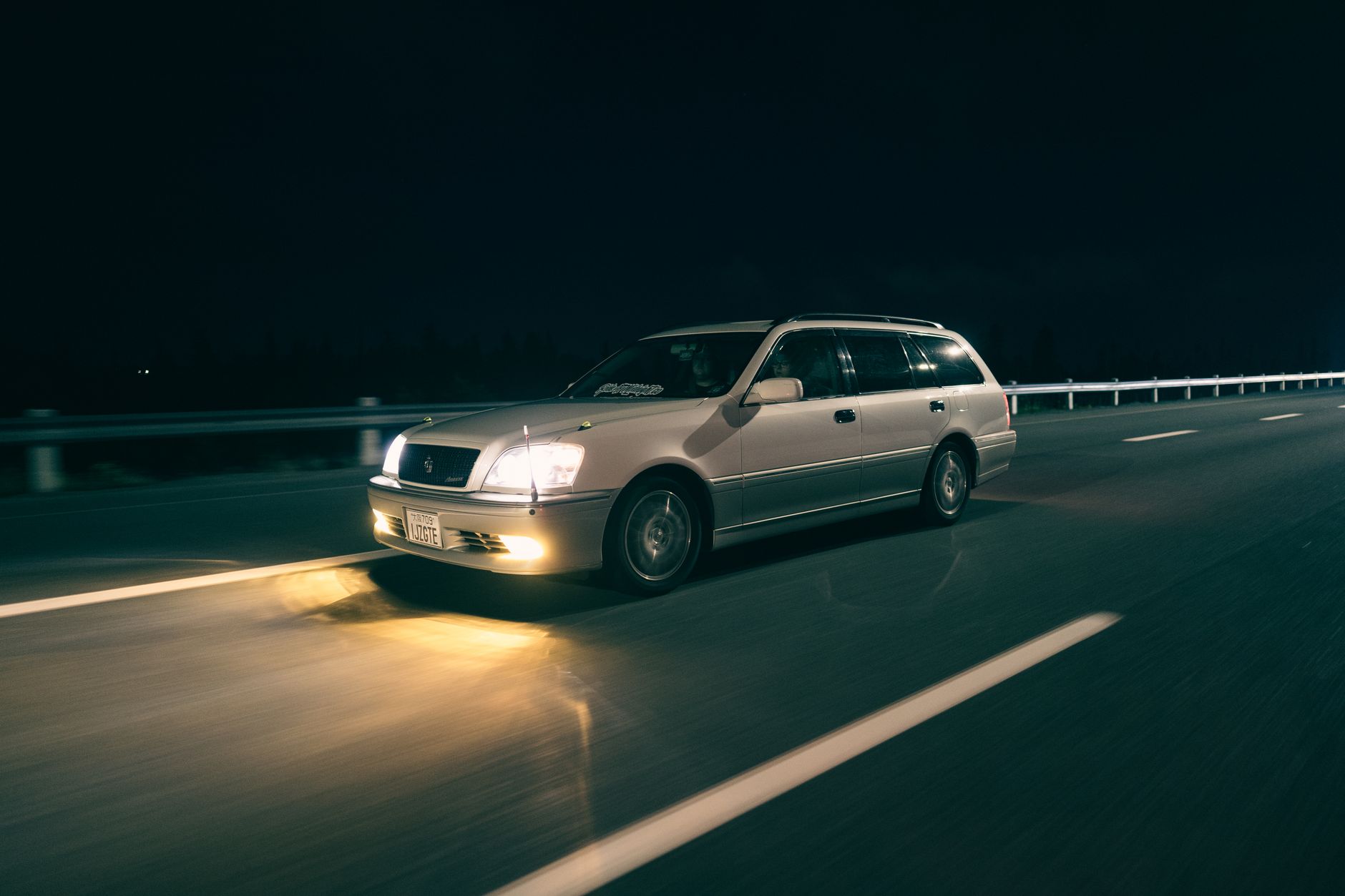 Voiture blanche roulant de nuit sur une route éclairée par ses phares.